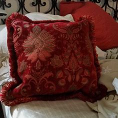 a red pillow sitting on top of a bed covered in blankets and pillows next to a metal headboard