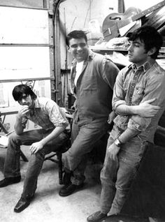 three men are sitting in front of a piano and looking at the camera while another man is standing behind them