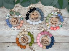 four key chains with different colored beads and charms on top of a wooden table next to leaves