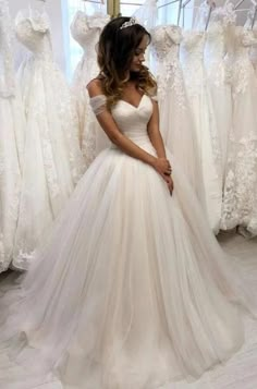 a woman in a white wedding dress standing next to some dresses on mannequins