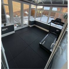 an indoor gym with treadmills and snow outside the windows, in front of a brick building