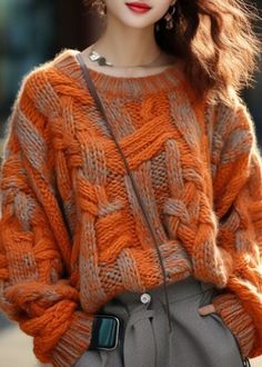 a woman wearing an orange sweater and grey pants with her hand on her hip, looking at the camera