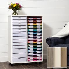 a white cabinet filled with lots of drawers next to a blue chair and flower pot