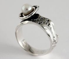 "Here is the ring \"Flower of sea\" in sterling silver and white freshwater pearl. Each ring is unique, the lace around the dome that hosts the pearl is unique each time and may be different from the photo. Size: 7 mm width (9/32 in) Material: Sterling silver and white freshwater pearl The unique texture of the ring is made from a molding of a sea urchin shell symbolizing a footprint of good times. This organic texture was handcrafted by the jeweler Marie-Eve Bordeleau of Trois-Rivières, Quebec, Canada. Included: -A polishing cloth -A bookmark about the collection -A rigid box ** Shipping fees are free in Canada and the United States Inspiration: The shell of the sea urchin inspires emotions, feelings and memories. The unique impressions left by the shells symbolize a true story, a trip or Unique Pearl Jewelry For Anniversary, Unique Pearl White Jewelry For Wedding, Elegant 925 Stamped Pearl Promise Ring, Elegant Silver Pearl Ring Stamped 925, Wedding Pearl Rings With Pearl Pendant, Elegant Sterling Silver Pearl Ring Stamped 925, Wedding Pearl Ring Stamped 925 In Sterling Silver, Wedding Pearl Ring In Sterling Silver, White Pearl Sterling Silver Ring