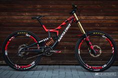 a red and black mountain bike parked in front of a wooden wall