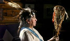 an old native american man holding a large stick with feathers on it's head