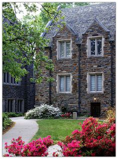 an old stone house with flowers in the foreground and walkway leading up to it