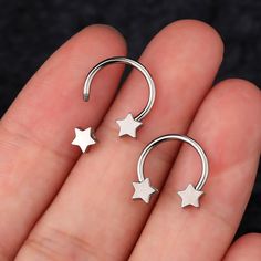 two small silver stars are attached to a nose piercing ring on someone's finger