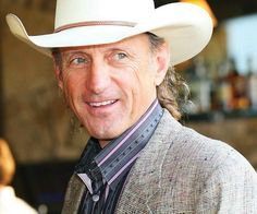 a man wearing a white cowboy hat smiling at the camera