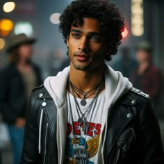 a young man with curly hair wearing a black leather jacket and white hoodie is looking at the camera