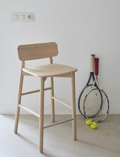 a wooden chair next to a tennis racket and ball on the floor in front of a white wall