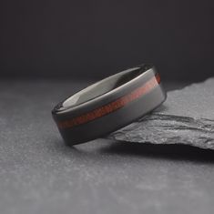 a wedding band with red wood inlays sits on top of a piece of rock