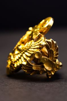 a gold ring with an eagle design on the front and side, sitting on a black surface