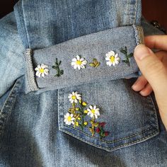 someone is stitching daisies on the back of their jean jacket