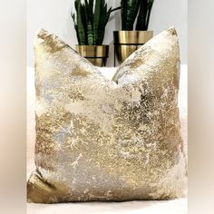 two potted plants sitting on top of a white table next to a gold pillow