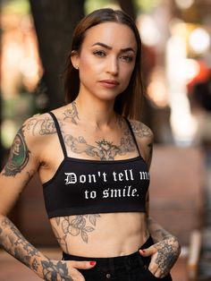 Witchwood Bags' Don't Tell Me To Smile bralette. This cute, black, and sporty bralette features a Don't Tell Me To Smile text graphic in white. Wear it on its own or under a shirt with shorts! Cotton Janice is wearing an extra-small Made in the United States Black Cotton Sports Bra With Built-in Bra, Black Cotton Sports Bra For Summer, Trendy Black Sports Bra, Trendy Sports Crop Top With Letter Print, Trendy Summer Streetwear Sports Bra, Trendy Streetwear Sports Bra For Summer, Trendy Sports Bra For Summer Streetwear, Trendy Summer Sports Bra For Streetwear, Summer Streetwear Sports Bra