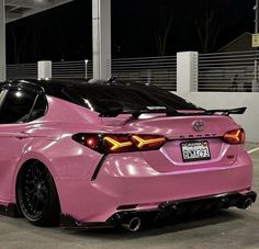 a pink toyota car parked in a parking lot at night with its hood up and tail lights on