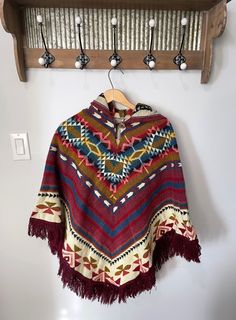 Infuse a touch of boho flair into your closet with our enchanting artisanal ponchos. Meticulously fashioned by our skilled craftsmen in Ecuador, these ponchos exhibit a pullover style accompanied by a hood, and they boast an unparalleled tribal pattern for a truly distinctive look. Dimensions:  Length: 32 in (with fringe 36 in) Width: 41 in ♥ Experience the comfort of our exquisite tribal ponchos, crafted for both warmth and durability to accompany you through your everyday adventures. OUR MISSI Bohemian Winter Cape One Size, Bohemian Winter Shawl Poncho, Bohemian Multicolor Poncho For Fall, Multicolor Bohemian Poncho For Fall, Bohemian Alpaca Cape For Fall, Hippie Brown Poncho For Winter, Bohemian Alpaca Shawl, Bohemian Alpaca Shawl For Fall, Bohemian Alpaca Cape For Winter