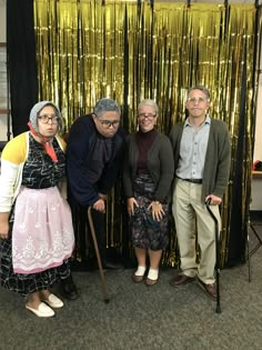 three older people standing next to each other in front of a gold foil curtain with a cane