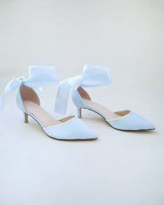 a pair of white high heeled shoes with a bow on the toe and side