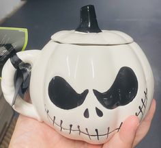 a hand holding a ceramic teapot decorated like a jack - o'- lantern