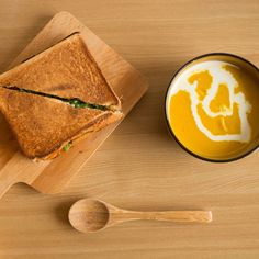 a bowl of soup next to a cut in half sandwich on a wooden cutting board