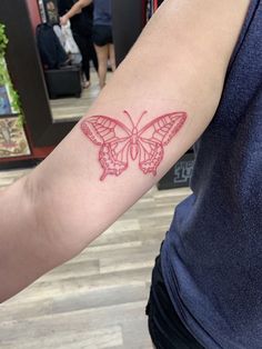 a red butterfly tattoo on the arm of a woman's left arm in a store