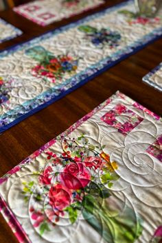 four quilted placemats with flowers on them sitting on a wooden table top