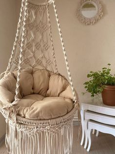 a white hanging chair next to a table and potted plant in a living room