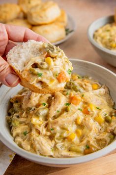 a hand holding a piece of bread over a bowl of chicken pot pie casserole