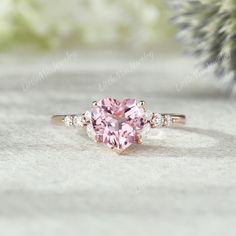 a pink heart shaped diamond ring with three diamonds on the band and side stones around it