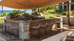 an outdoor bar with chairs and umbrellas next to the ocean