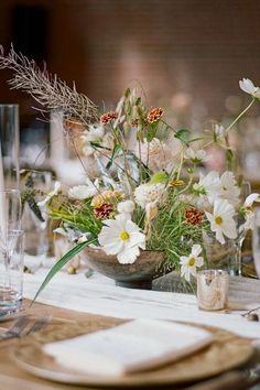 an arrangement of flowers in a bowl on a table with place settings and napkins