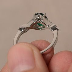 a close up of a person's hand holding a ring with a green stone