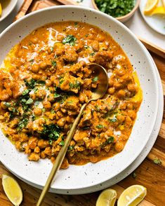 a white bowl filled with meat and garnished with cilantro, parsley and lemon wedges