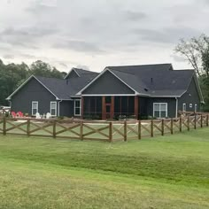 a large gray house sitting on top of a lush green field next to a wooden fence