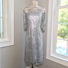 a silver dress on a mannequin stand in front of a white wall and window