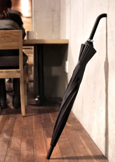 an open black umbrella sitting on top of a wooden floor next to a woman in a chair