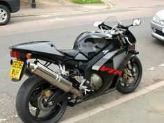 a black motorcycle parked on the side of the road next to a silver car and another vehicle