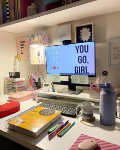 a desk with a computer monitor, keyboard and notebook on it next to other office supplies