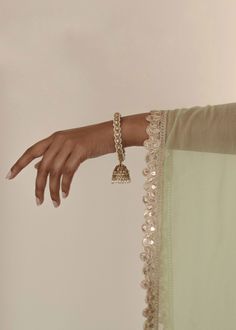 Adorn your wrists with the refined elegance of our antique gold Saavana Bangles, featuring almond-shaped gems and cream stones. The dangling jhumkas add a touch of sophistication, perfect for standalone chic or curated bangle ensembles. Includes 2 bangles. Elegant Kundan Sharara For Transitional Seasons, Traditional Sharara With Intricate Design For Festive Occasions, Elegant Brass Jhumkas For Festive Occasions, Elegant Brass Jhumkas For Festive Season, Elegant Silver Sharara For Festivals, Wedding Brass Chandbalis With Tilla Detailing, Wedding Brass Chandbalis With Tilla, Wedding Chandbalis In Brass With Tilla Detail, Wedding Chandbalis With Tilla In Brass