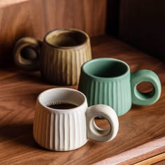 three ceramic coffee cups sitting on top of a wooden table next to each other,