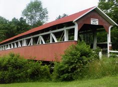 an old covered bridge sits in the middle of some trees and bushes on a cloudy day