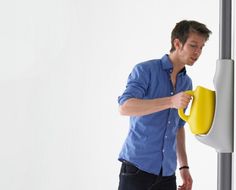 a man holding a yellow cup in his right hand while standing next to a white wall