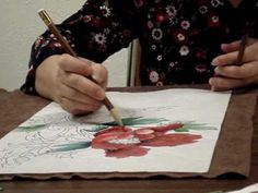 a woman is drawing on paper with a pencil and watercolor pen while sitting at a table