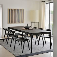 a dining table with six chairs and a vase on it in front of a large window