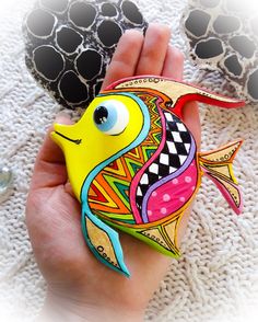 a hand holding a brightly colored fish brooch