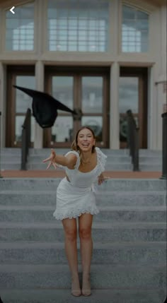 a woman in a white dress is standing on some steps and throwing a graduation cap into the air