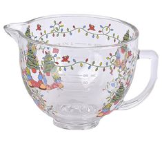 a glass mixing bowl with christmas decorations on the rim and handles, decorated with holly