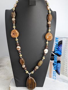 Here is another statement necklace from our collection! It is comprised of brown and tan beads ranging from wood, mosaic glass, tiger's eye, gold toned acrylic, brown quartz, and silver acrylic beads. The pendant is tiger's eye and it was delicately sourced by a member of the Artisan Queens. The clasp is a lobster claw and it's tough enough to withstand this 9 ounce stunner. Check out the rest of our collection for more present and future statement pieces! Happy shopping! Luxury Brown Beaded Necklaces In Elegant Style, Unique Brown Beaded Necklace With Polished Beads, Nature-inspired Brown Beaded Necklace, Brown Polished Beads For Jewelry Making, Brown Beaded Long Necklace Gift, Brown Beaded Long Necklace For Gift, Unique Brown Polished Beads, Brown Agate Beads For Jewelry Making, Brown Wooden Beads Long Necklace